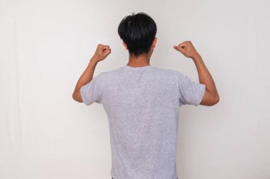 Kutlamada yumruğunu sıkan genç bir Asyalı 'nın arka planda beyaz bir arka planda duruşu başarıyı, motivasyonu ve başarıyı sembolize ediyor.