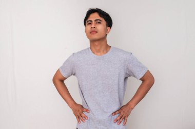 Belini tutan ve beyaz izole bir arka planda kızgın bir ifadeyle kameraya bakan Asyalı genç bir adamın portresi. Duygular ve tutumlar için mükemmel.