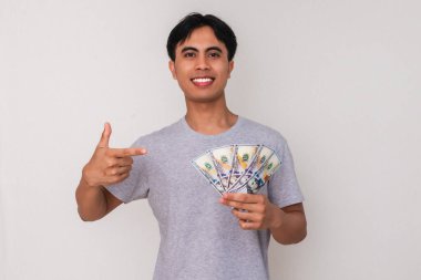 Asyalı mutlu genç adam ayakta ve elinde neşeli bir ifadeyle, beyaz arka planda soyutlanmış bir şekilde para tutuyor. Finans, iş ya da reklam kavramları için mükemmel