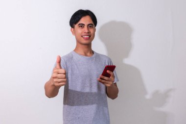 Beyaz arka planda izole edilmiş akıllı telefonu tutan gülümseyen Asyalı genç adam. Terfi için, mobil reklamlar için ya da teknolojiyle ilgili kampanyalar için mükemmel.