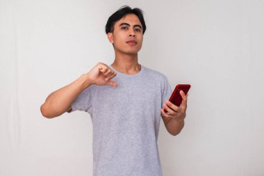 Beyaz arka planda izole edilmiş akıllı bir telefonu tutan kendine güvenen Asyalı genç bir adam. Promosyon, kişisel markalaşma veya mobil reklam kavramları için mükemmel.