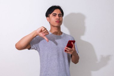Hayal kırıklığına uğramış genç Asyalı bir adam elinde akıllı bir telefonla, beyaz arka planda izole edilmiş, reklam, teknoloji ve tepki kavramları için mükemmel.