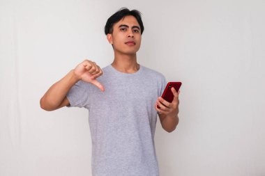 Hayal kırıklığına uğramış genç Asyalı bir adam elinde akıllı bir telefonla, beyaz arka planda izole edilmiş, reklam, teknoloji ve tepki kavramları için mükemmel.