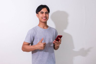 Beyaz arka planda izole edilmiş akıllı telefonu tutan gülümseyen Asyalı genç adam. Terfi için, mobil reklamlar için ya da teknolojiyle ilgili kampanyalar için mükemmel.