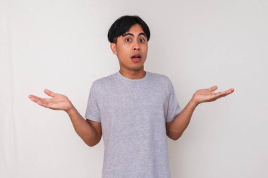 Genç Asyalı adam, beyaz arka planda güvensiz ve izole bir şekilde ellerini kaldırarak karışık bir 