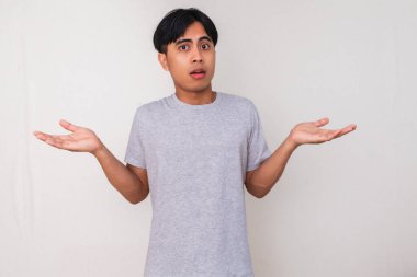 Genç Asyalı adam, beyaz arka planda güvensiz ve izole bir şekilde ellerini kaldırarak karışık bir 