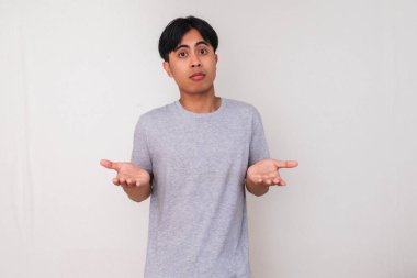 Genç Asyalı adam, beyaz arka planda güvensiz ve izole bir şekilde ellerini kaldırarak karışık bir 