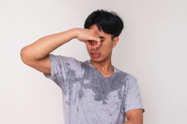 Genç Asyalı bir adam vücut kokusundan tiksinerek terliyor ve burnunu kapatıyor, beyaz arka planda izole edilmiş, hijyen ve deodorant reklamı için mükemmel.
