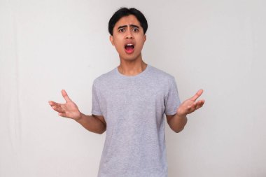 Beyaz arka planda izole edilmiş, ciddi bir ifadeyle kameraya bakan kızgın bir Asyalı gencin portresi. Reklamlar, duygular ve iletişim kavramları için mükemmel.