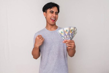 Kutlamada elinde para tutan ve yumruğunu sıkan mutlu Asyalı genç bir adamın portresi, izole edilmiş beyaz bir arka plana karşı neşeyle gülümsüyor, reklam için mükemmel.