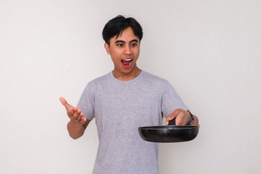 Elinde tuttuğu kızartma tavasına bakan heyecanlı bir Asyalı adamın portresi, beyaz arka planda izole edilmiş, yemek, ya da yaşam tarzı kavramları için ideal.