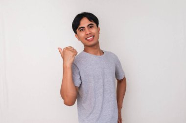 Gülümseyen genç bir Asyalı 'nın portresi beyaz izole bir arka planda başparmağıyla yan tarafı işaret ediyor. Reklam, promosyon ve sunum modeli için mükemmel.