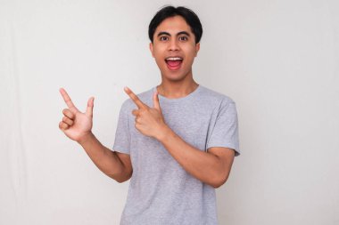 Heyecanlı genç Asyalı adam, temiz, izole edilmiş beyaz bir arka planda, ürün ya da hizmet reklamı için çalışma alanı gösteriyor.