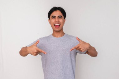 Asyalı genç bir adamın portresi iki eliyle aşağıya bakıyor ve heyecanlı bir yüz ifadesi sergiliyor, beyaz arka planda izole edilmiş, reklam ve promosyonlar için mükemmel.