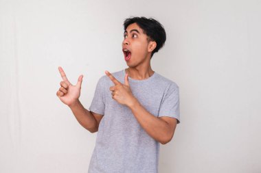 Yüzünde tuhaf bir ifade olan, beyaz arka planda izole edilmiş, promosyon veya reklam içeriği için mükemmel genç Asyalı bir adamın portresi.