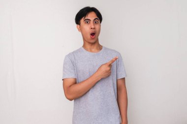 Yüzünde tuhaf bir ifade olan, beyaz arka planda izole edilmiş, promosyon veya reklam içeriği için mükemmel genç Asyalı bir adamın portresi.