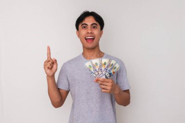 Elinde para olan genç bir Asyalı 'nın portresi heyecanlı bir ifadeyle beyaz arka planda izole edilmiş, reklamlar ve finansal promosyonlar için mükemmel.