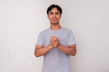 Genç Asyalı bir adamın portresi, beyaz arka planda kendi ellerini tutarken nazikçe gülümsüyor.