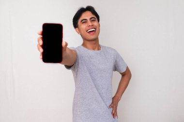 Mutlu genç Asyalı bir adam kameraya boş bir cep telefonu ekranı gösterirken beyaz izole bir arka planda gülümsüyor. Reklam veya dijital yaşam tarzı içeriği için stüdyo portresi