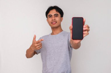 Mutlu genç Asyalı bir adam kameraya boş bir cep telefonu ekranı gösterirken beyaz izole bir arka planda gülümsüyor. Reklam veya dijital yaşam tarzı içeriği için stüdyo portresi