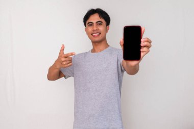 Mutlu genç Asyalı bir adam kameraya boş bir cep telefonu ekranı gösterirken beyaz izole bir arka planda gülümsüyor. Reklam veya dijital yaşam tarzı içeriği için stüdyo portresi