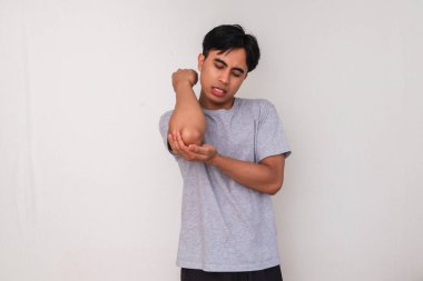 Dirseğini, sağlık, acı ve hastalıkla ilgili içerik için uygun beyaz bir arka planda tutarken acı çeken genç bir Asyalı adamın portresi.