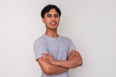 Kollarını kavuşturup kameraya temiz beyaz arka planda bakan kendine güvenen genç Asyalı bir adamın portresi iş, promosyon ya da reklam teması için mükemmel.