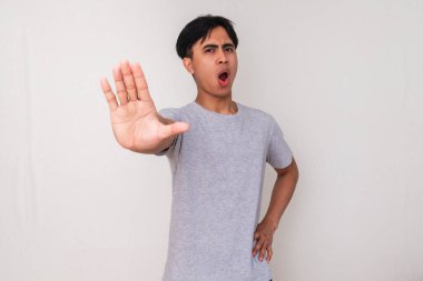 Beyaz bir arka planda izole bir şekilde kameraya bakarken el hareketi yapan Asyalı genç bir adamın portresi. Uyarı ve bilinçlendirme kampanyaları için mükemmel