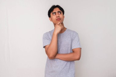 Asyalı genç bir adamın portresi, eli çenesinde ve gözlerinde, beyaz arka planda soyutlanmış, yaratıcı reklam veya konsept çizimi için mükemmel bir şekilde ciddi bir şekilde düşünüyor.