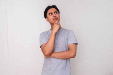 Asyalı genç bir adamın portresi, eli çenesinde ve gözlerinde, beyaz arka planda soyutlanmış, yaratıcı reklam veya konsept çizimi için mükemmel bir şekilde ciddi bir şekilde düşünüyor.