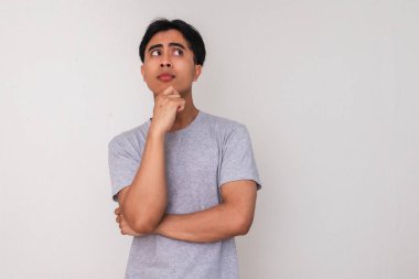 Asyalı genç bir adamın portresi, eli çenesinde ve gözlerinde, beyaz arka planda soyutlanmış, yaratıcı reklam veya konsept çizimi için mükemmel bir şekilde ciddi bir şekilde düşünüyor.