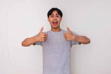 Genç bir Güneydoğu Asyalı 'nın portresi. Heyecanlı ve mutlu bir yüzü olan, temiz beyaz bir arkaplana karşı duran iki baş parmağını gösteriyor. Reklamlar, tanıtımlar ve başarı kavramları için mükemmel.