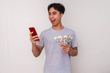 Elinde para tutarken akıllı telefonuna bakan, beyaz arka planda izole edilmiş mutlu bir Güneydoğu Asyalı adamın portresi. Reklam, finans ve dijital ödeme temaları için mükemmel
