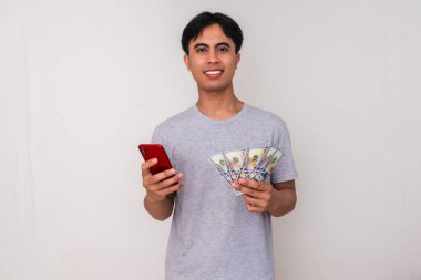 Elinde para tutarken akıllı telefonuna bakan, beyaz arka planda izole edilmiş mutlu bir Güneydoğu Asyalı adamın portresi. Reklam, finans ve dijital ödeme temaları için mükemmel