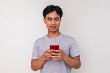 Beyaz arka planda akıllı telefonunu kullanırken gülümseyen genç Güneydoğu Asyalı bir adamın portresi dijital reklamlar, promosyonlar veya modern iletişim temaları için mükemmel.