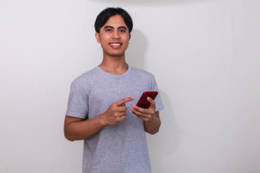 Beyaz arka planda akıllı telefonunu kullanırken gülümseyen genç Güneydoğu Asyalı bir adamın portresi dijital reklamlar, promosyonlar veya modern iletişim temaları için mükemmel.