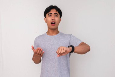 İzole edilmiş beyaz bir arka planda, şok olmuş bir ifadeyle saatine bakan Asyalı genç bir adamın portresi. Zaman kavramları, aciliyet ya da son dakika hatırlatması için mükemmel.