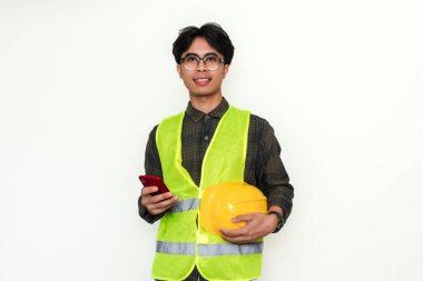 Gülümseyen genç Asyalı mühendis kendine güvenen bir akıllı telefon tutuyor. Modern teknolojiye sahip bir profesyonelin portresi, farklı endüstri kavramları için idealdir.