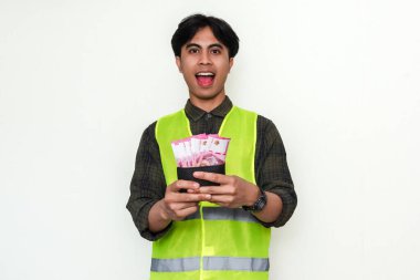 Mutlu Asyalı inşaat işçisi para dolu cüzdana bakıp heyecanlı bir yüz ifadesi göstererek beyaz arka planda izole edilmiş bir şekilde hayrete düştü. Maaş, ödül ve başarı temaları için ideal