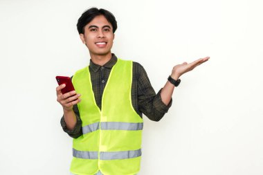 Akıllı telefon tutan Asyalı mutlu inşaat işçisi ve beyaz arka planda izole edilmiş bir avuç içi hareketi gösteriyor. Reklam, iletişim ve teknoloji temaları için ideal