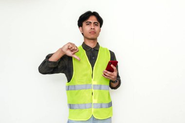 Hayal kırıklığına uğramış Asyalı inşaat işçisi akıllı telefon tutarken beyaz arka planda izole edilmiş baş parmak hareketi gösteriyor. Olumsuz eleştiriler ya da kötü hizmet reklam temaları için mükemmel