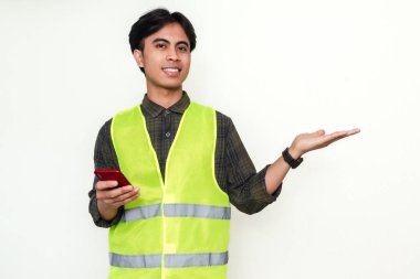 Akıllı telefon tutan Asyalı mutlu inşaat işçisi ve beyaz arka planda izole edilmiş bir avuç içi hareketi gösteriyor. Reklam, iletişim ve teknoloji temaları için ideal