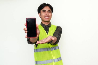 Mutlu Asyalı inşaat işçisi kameraya beyaz arka planda izole edilmiş neşeli bir ifadeyle boş akıllı telefon ekranı gösteriyor. Mobil uygulama veya reklam konsepti için mükemmel