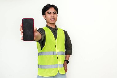 Mutlu Asyalı inşaat işçisi kameraya beyaz arka planda izole edilmiş neşeli bir ifadeyle boş akıllı telefon ekranı gösteriyor. Mobil uygulama veya reklam konsepti için mükemmel