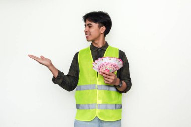 Gülümseyen Asyalı inşaat işçisi elinde nakit para tutuyordu ve beyaz arka planda izole edilmiş mutlu bir ifadeyle avuç içi gösteriyordu. Maaş, başarı veya finansal özgürlük kavramları için mükemmel.