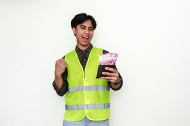 Heyecanlı Asyalı inşaat işçisi para dolu cüzdana bakarken başarıyı neşeli bir ifadeyle kutluyor, beyaz arka planda izole edilmiş.