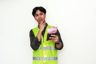 Asyalı inşaat işçisi para dolu cüzdanı tutarken beyaz arka planda izole edilmiş bir jest yapıyor. Finans, maaş veya maaşla ilgili içerik için mükemmel