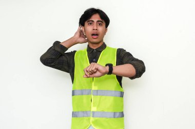 Asyalı stresli bir inşaat işçisinin portresi saatine paniklemiş bir ifadeyle bakıyor, beyaz bir arka planda izole edilmiş. Zaman baskısı ve zaman sınırı kavramları için mükemmel.