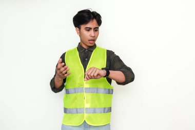 Kafası karışmış Asyalı bir inşaat işçisinin portresi beyaz arka planda izole edilmiş saatine bakıyor. Yapımda son teslim tarihi, gecikme ya da zaman baskısı gibi kavramlar için mükemmel