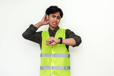 Kafası karışmış Asyalı bir inşaat işçisinin portresi beyaz arka planda izole edilmiş saatine bakıyor. Yapımda son teslim tarihi, gecikme ya da zaman baskısı gibi kavramlar için mükemmel